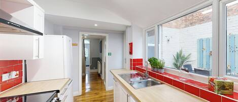 Una cocina moderna con piso de madera, electrodomésticos de acero inoxidable y un salpicadero rojo.