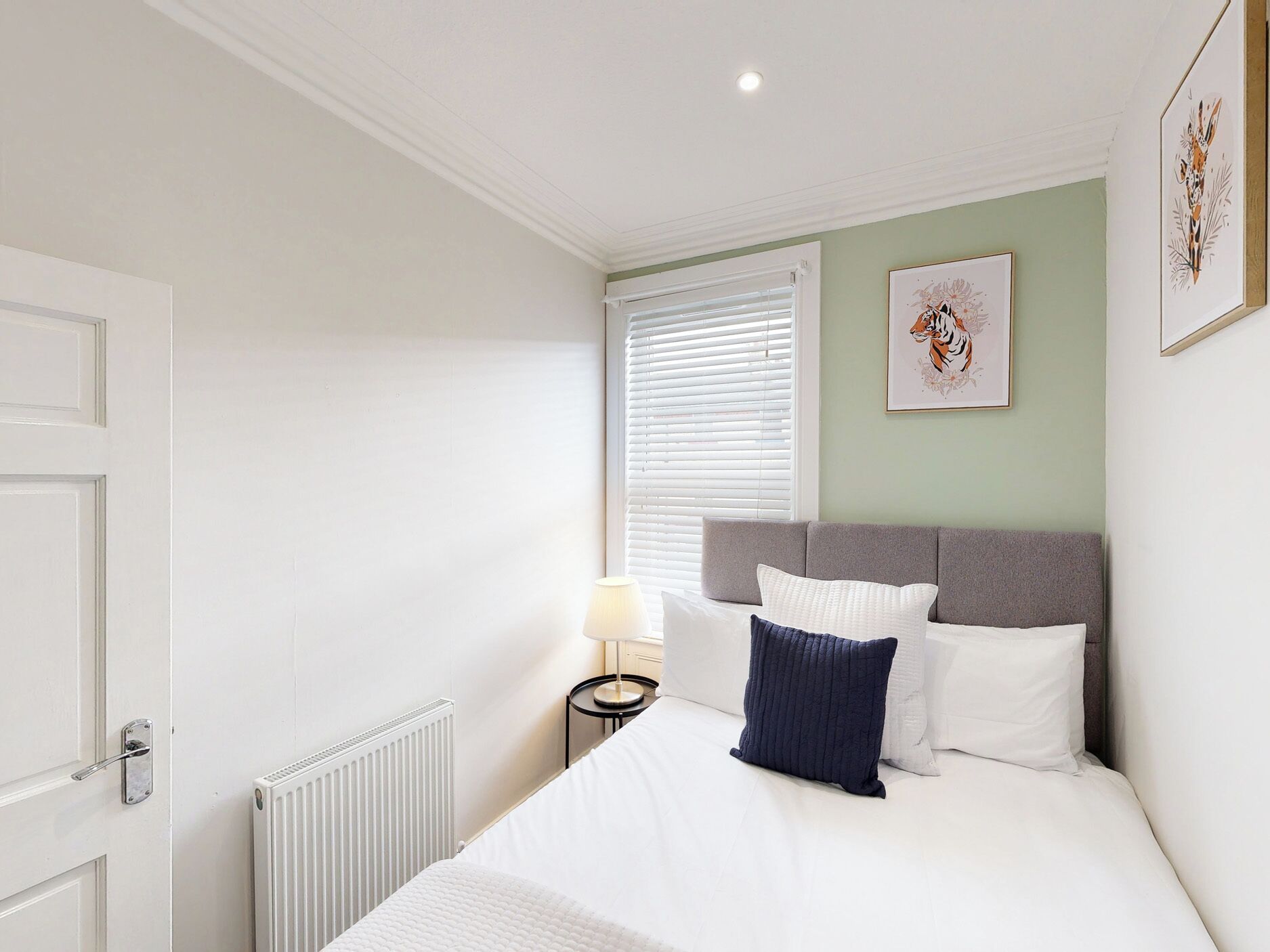 A bedroom with a bed, a nightstand, a lamp, and a window with blinds.