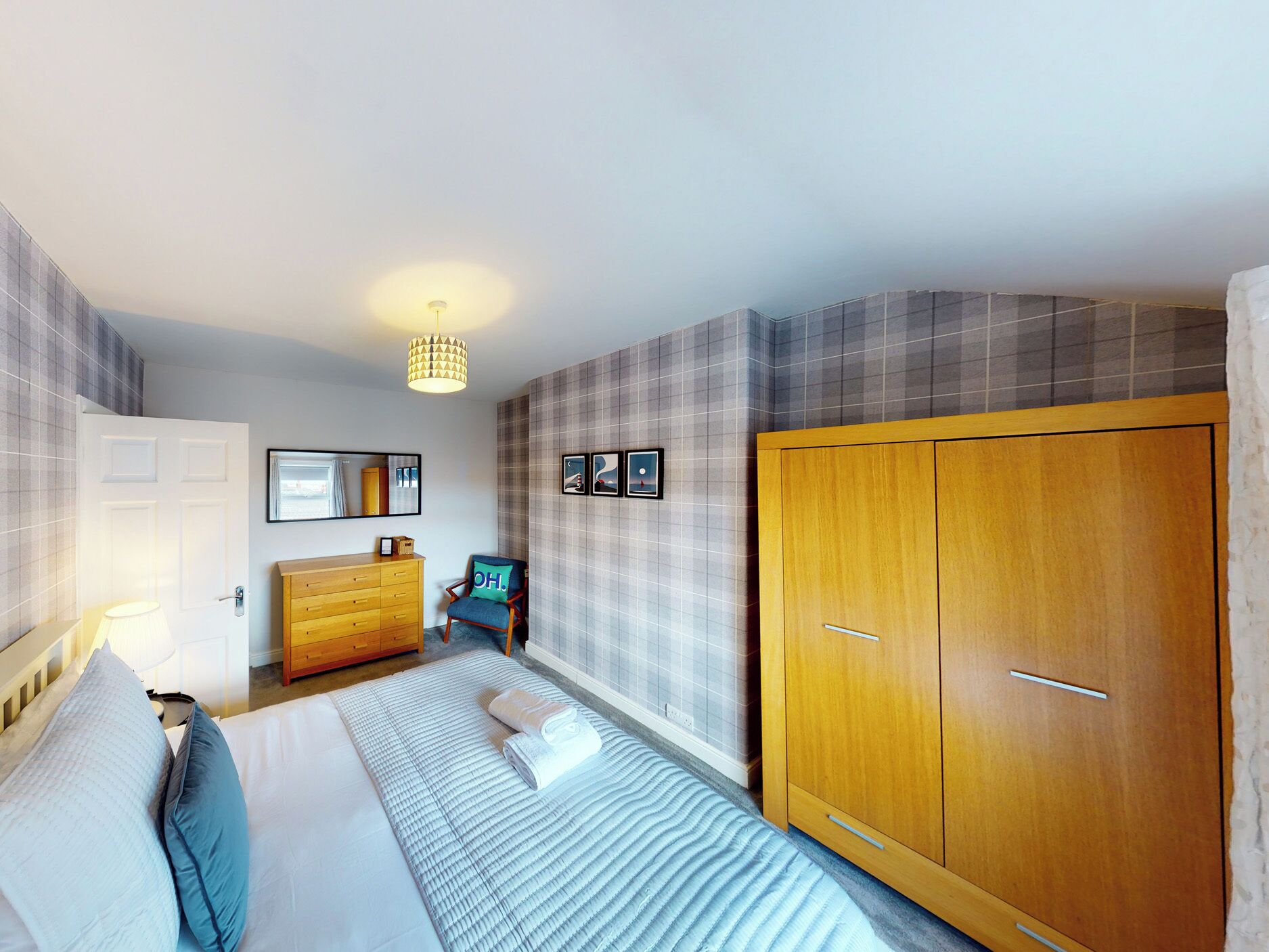 A bedroom with a bed, a wooden wardrobe, a dresser, a chair, and a wall-mounted lamp.