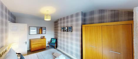 A bedroom with a bed, a wooden wardrobe, a dresser, a chair, and a wall-mounted lamp.