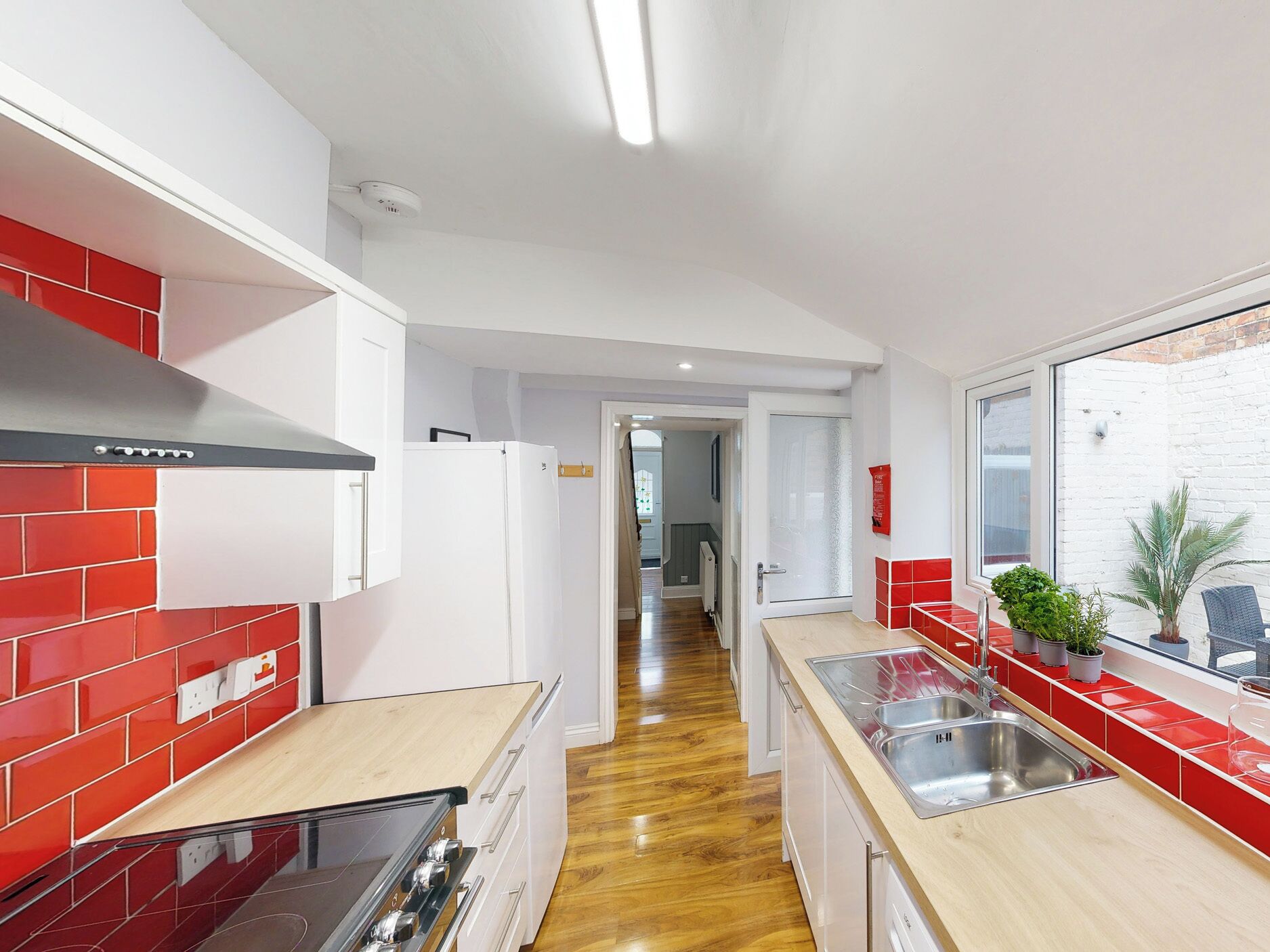 Una cocina moderna con baldosas rojas y blancas, electrodomésticos de acero inoxidable y encimera de madera.