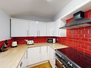 Cocina compacta con armarios blancos, salpicadero de azulejos rojos, microondas, tostadora y estufa.
