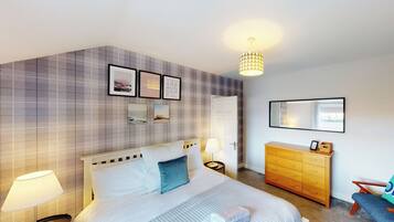 A hotel room with a bed, bedside tables, a dresser, a mirror, and a wall with framed pictures.