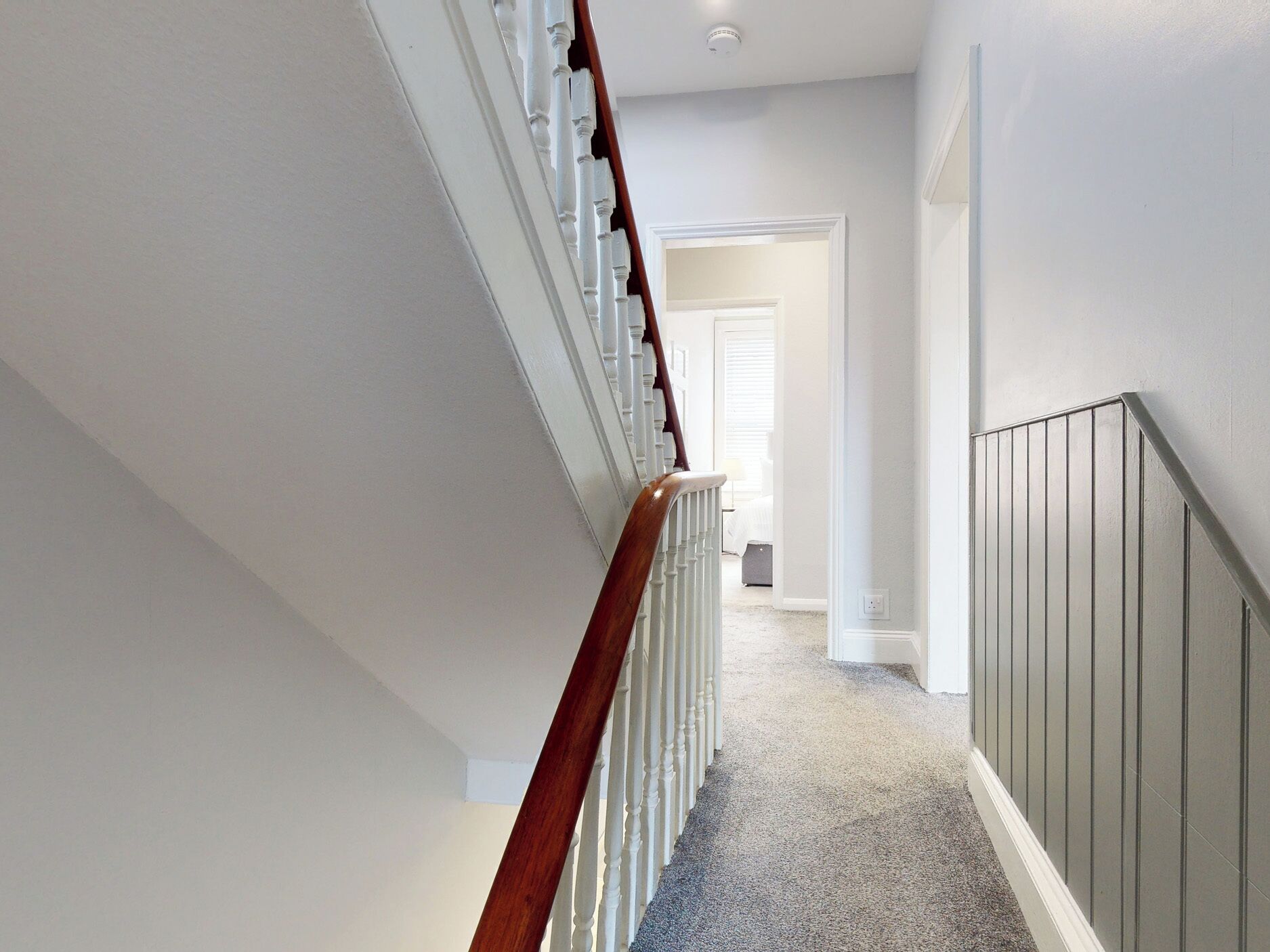 A clean, narrow hallway with a wooden staircase on one side and a grey wall on the other.