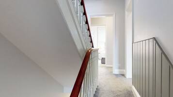 A clean, narrow hallway with a wooden staircase on one side and a grey wall on the other.