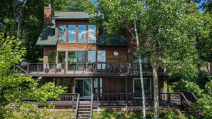 A two-story wooden cabin with a balcony, surrounded by trees. - Edgewater Haven on Lake Chetac (Birchwood)