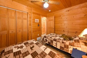 A wooden cabin room with two beds, a ceiling fan, and a door leading to another room. - Edgewater Haven on Lake Chetac (Birchwood)