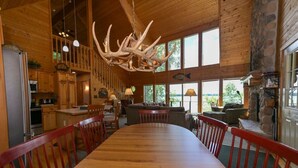 A spacious dining area with a long wooden table and red chairs, a kitchen with wooden cabinets, and a stone fireplace. - Edgewater Haven on Lake Chetac (Birchwood)