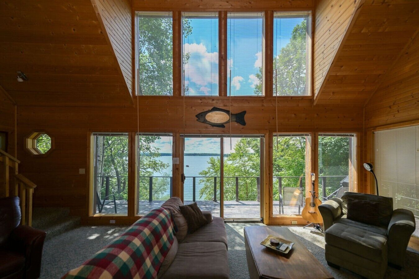 L’intérieur d’une cabane, avec une grande porte-fenêtre à l’avant, un canapé, une table basse et un poisson décoratif accroché au mur.
