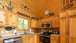 A wooden cabin kitchen with a stainless steel dishwasher, a microwave, an oven, and a sink. - Edgewater Haven on Lake Chetac (Birchwood)