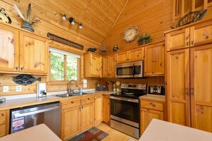 Eine Holzhütte mit einer Küche, ausgestattet mit einem Edelstahl-Geschirrspüler, einer Mikrowelle, einem Backofen und einem Spülbecken.