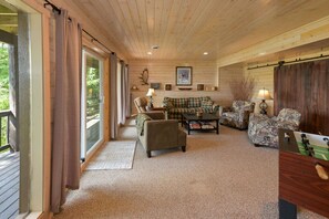 A cozy cabin interior with a wooden ceiling, a sofa, two armchairs, a coffee table, and a futon. - Edgewater Haven on Lake Chetac (Birchwood)