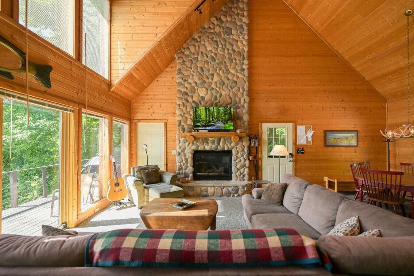 Ein gemütliches Blockhaus-Interieur mit Kamin aus Stein, Holzwänden, einem großen Fenster und einem Essbereich.