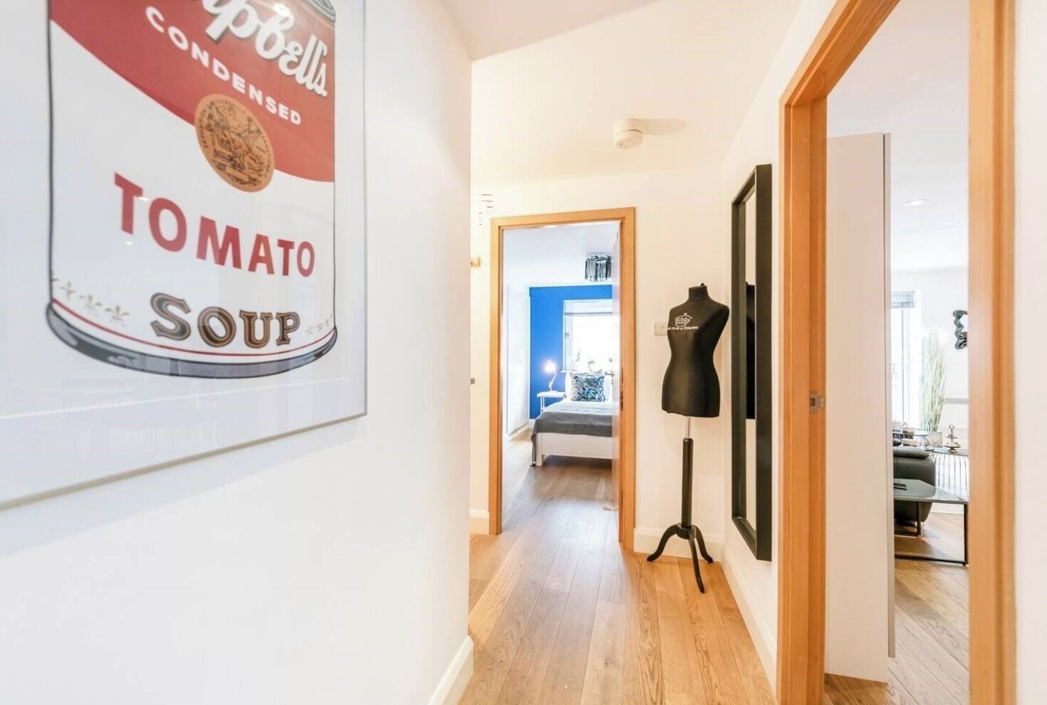 A hallway with a poster of a tomato soup can, a black mannequin, and a bed in the background.