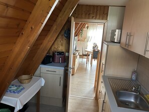 Eine kompakte Küche mit Holzbalkendecke, ein Essbereich mit Tisch und Stühlen sowie ein Blick in den Speisesaal.