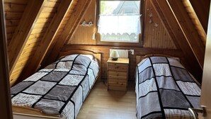 Ein kleines Dachzimmer mit zwei Einzelbetten, einem Holzkommode und einem Fenster mit Blick.