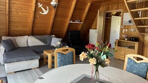 Ein gemütliches Schlafzimmer im Loft-Stil mit Schlafplatz in der ersten Etage, einem kleinen Tisch mit Blumenvase und einem Holzstuhl.