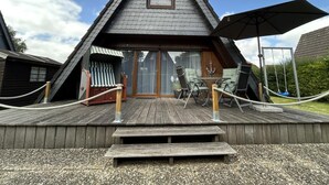 Ein dreieckiges Holzgebäude mit einer Terrasse, Sitzgelegenheiten im Freien und einem Seilgeländer.
