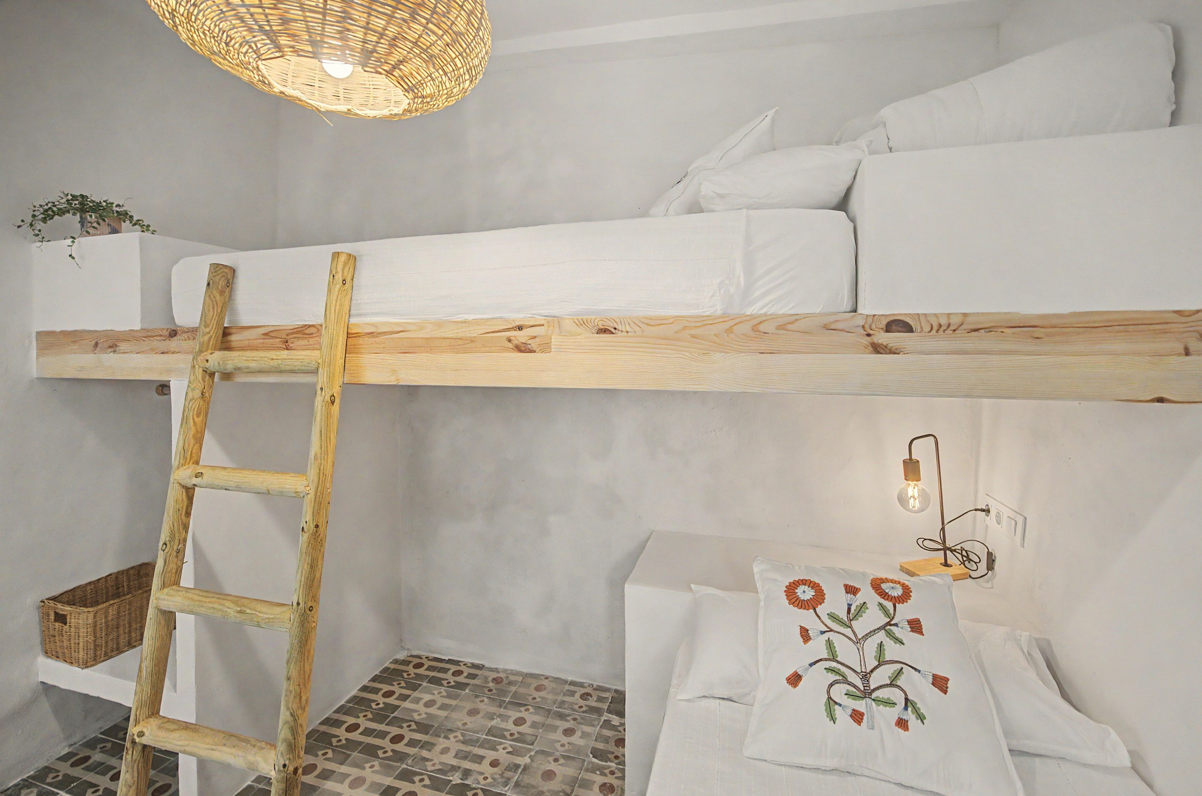A bunk bed with a wooden ladder, a wall-mounted light fixture, and a decorative pillow with a floral design.