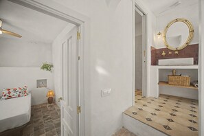 A hallway with a white door, a small bedside table with a floral pillow, a wall-mounted lamp, and a tiled floor. - Village House in the Town Center with Sea Views (Vejer de la Frontera)