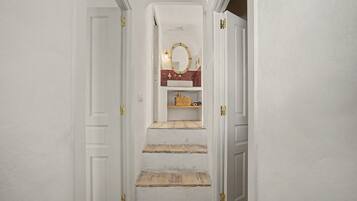 Un pasillo estrecho con paredes blancas y una escalera de madera que conduce a una habitación con un espejo y una repisa.