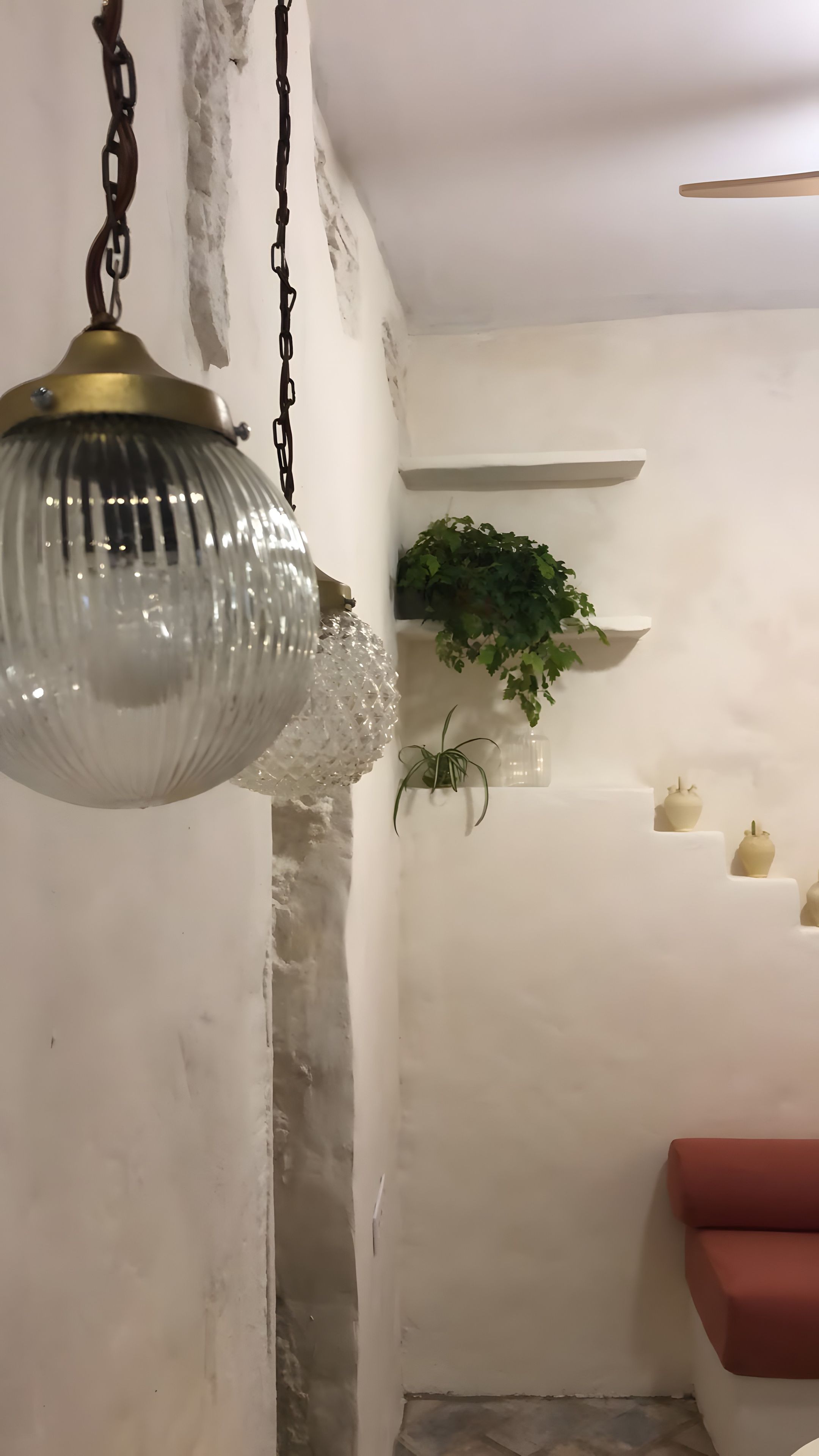 A room with a hanging light fixture, a plant on a shelf, and a red couch.