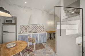 A kitchen with a microwave, a refrigerator, a wooden table with a bowl, and a staircase leading to an upper level. - Village House in the Town Center with Sea Views (Vejer de la Frontera)