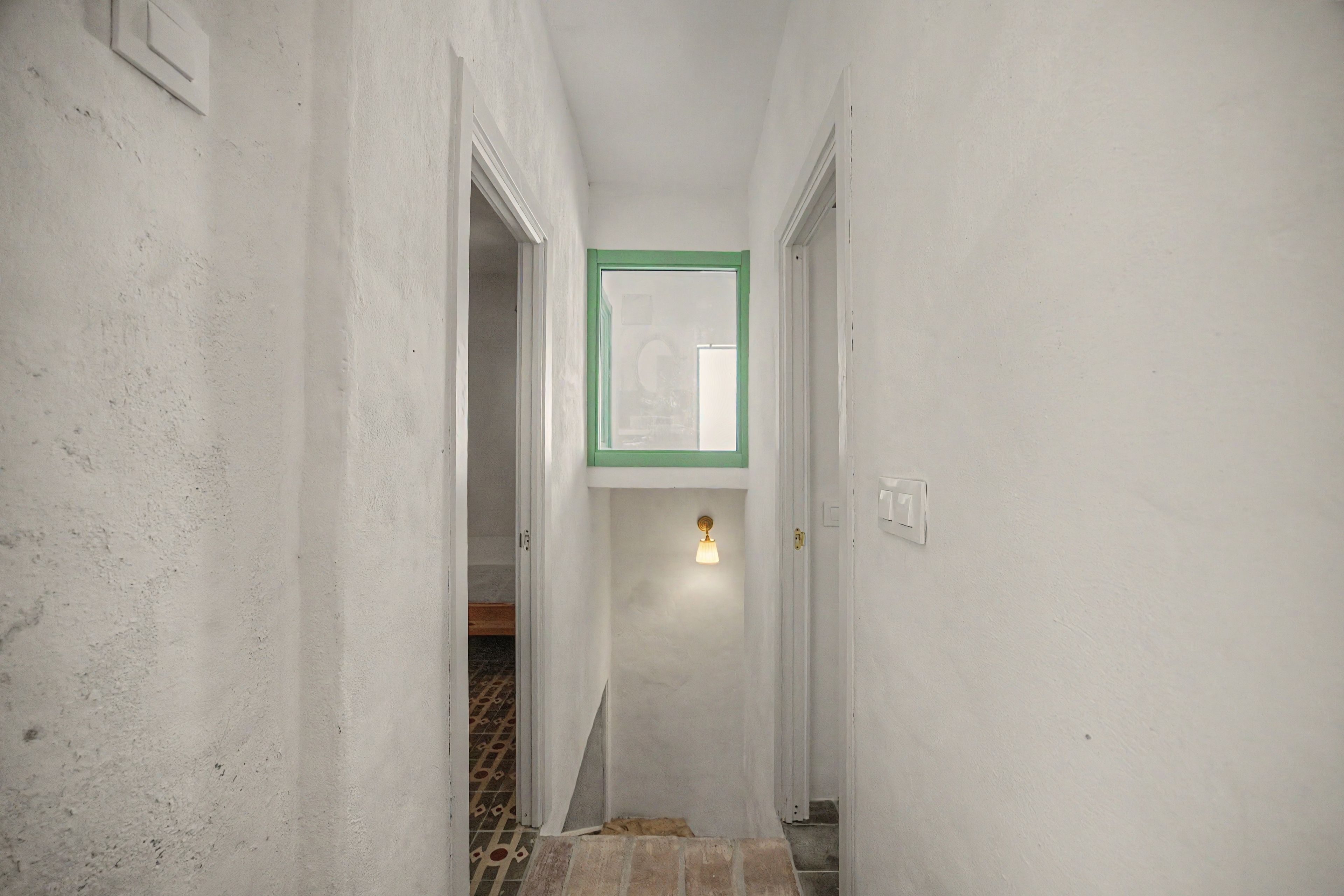 Un pasillo estrecho con paredes blancas, un marco de puerta visible y un accesorio de luz en la pared.