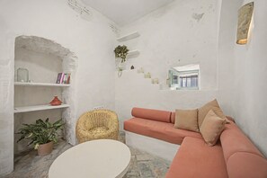 A living room with a white sofa, a round coffee table, and a wicker chair. There are shelves with books and decorative items, and a potted plant. - Village House in the Town Center with Sea Views (Vejer de la Frontera)