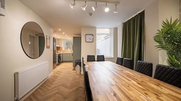 Uma sala de jantar com mesa de madeira, cadeiras estofadas pretas, um espelho redondo, um relógio e um vaso com planta.