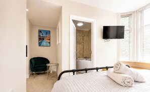 A hotel room with a bed, a TV, a shower, a chair, and a painting. - 127 Columbus Ravine (Scarborough)
