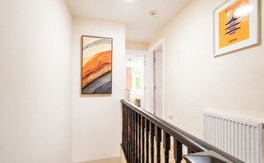 Ein Flur mit einer Holztreppe, einem gerahmten Gemälde und einem Poster an der Wand.