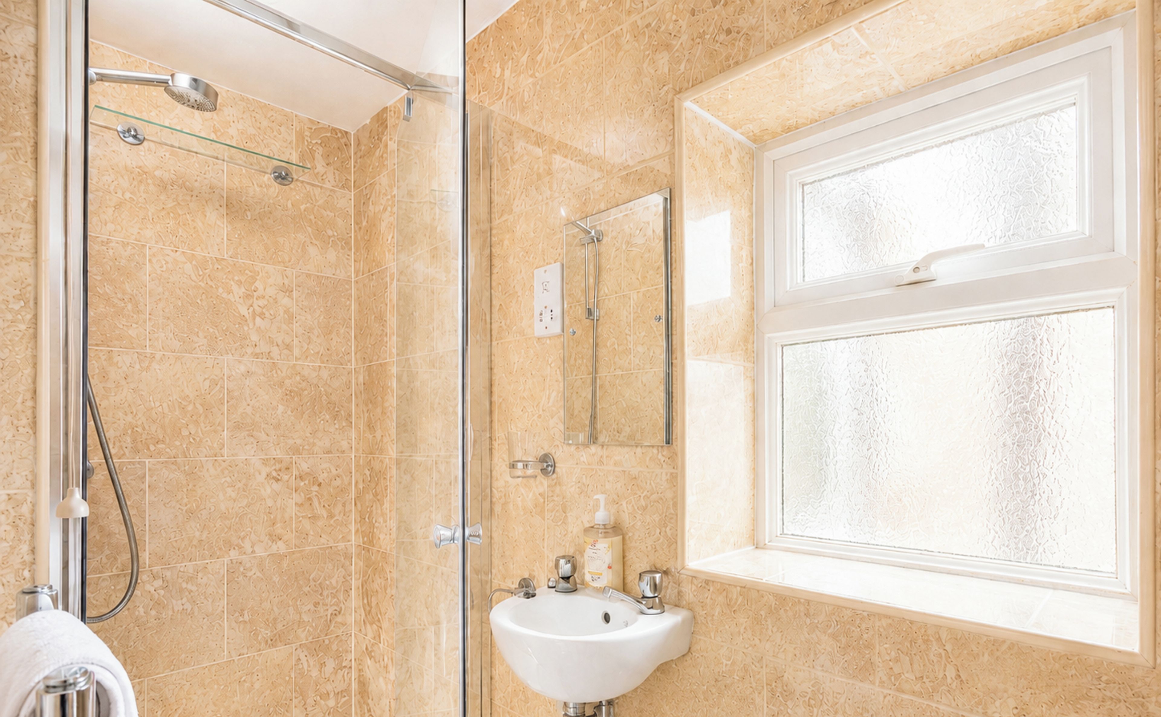 A bathroom with a glass shower enclosure, a sink with a mirror above it, and a window with frosted glass.