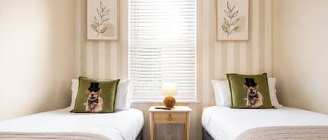 Habitación de hotel con dos camas, una mesita de noche con lámpara y una ventana con persianas.