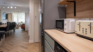 Una cocina moderna con refrigerador, microondas y tostadora. Hay una encimera de madera y una zona de comedor al fondo.