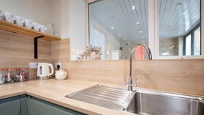 Una cocina moderna con un lavamanos de acero inoxidable, una tetera y frascos sobre la encimera.