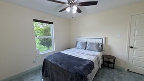 Un dormitorio con cama, ventilador de techo, ventana y puerta.
