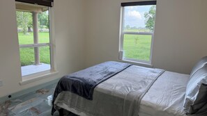 A bedroom with a bed, two windows, and a view of a green field.