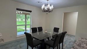 A conference room with a glass table, black chairs, a chandelier, and a window with a view of greenery.