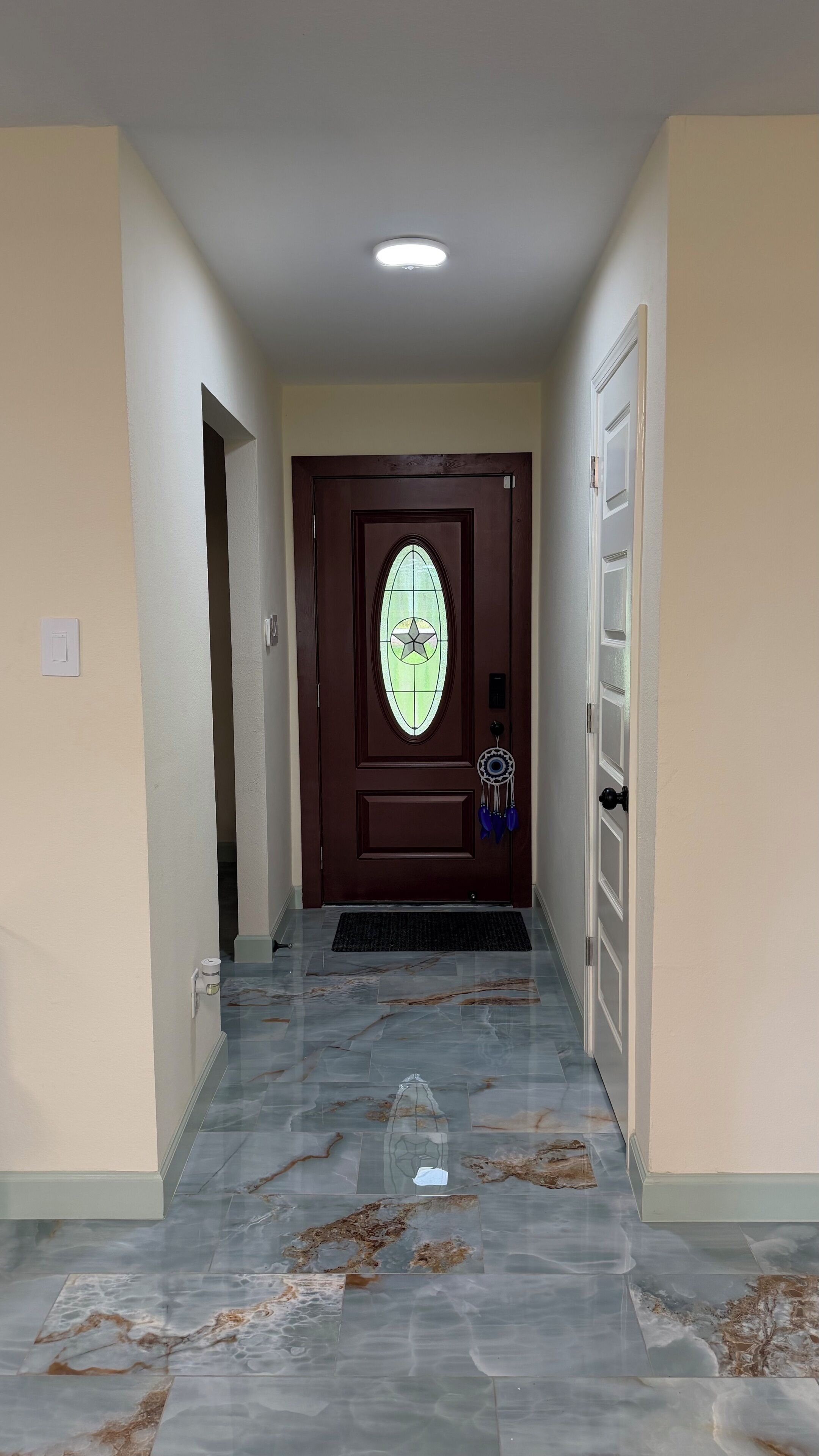 Un corridoio con pavimento in marmo, una porta marrone con un pannello di vetro e una decorazione a dreamcatcher.