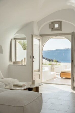 Ein modernes Schlafzimmer mit einem großen Bett, einem Nachttisch und einer offenen Tür, die auf einen Balkon mit Meerblick führt.