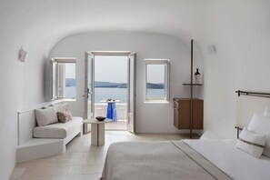 Ein modernes Schlafzimmer mit Bett, einer Couch, einem kleinen Tisch und Meerblick durch große Fenster.