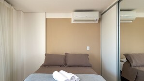 A hotel room with a bed, a window with curtains, an air conditioning unit, and a mirror. - Flat Near Flamboyant Mall - Bft3207 (Goiânia)