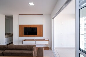 Ein modernes Wohnzimmer mit Flachbildfernseher an einer Holzvertäfelung, einer Couch und einem kleinen Tisch mit Fernbedienung.