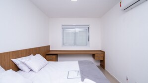 Una camera d'albergo moderna con un letto, comodini, una finestra con tende e un condizionatore.