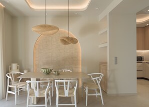 A modern dining area with a round table, white chairs, and two hanging light fixtures. - Infinity Suites 1, By Hellocrete (Rethymno)