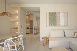 A modern living room with a sofa, a dining table with chairs, and a kitchen area in the background. - Infinity Suites 1, By Hellocrete (Rethymno)