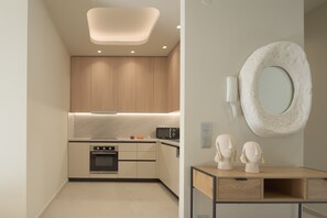 A modern kitchen with built-in appliances, a wooden cabinet, and a unique wall-mounted mirror. - Infinity Suites 1, By Hellocrete (Rethymno)