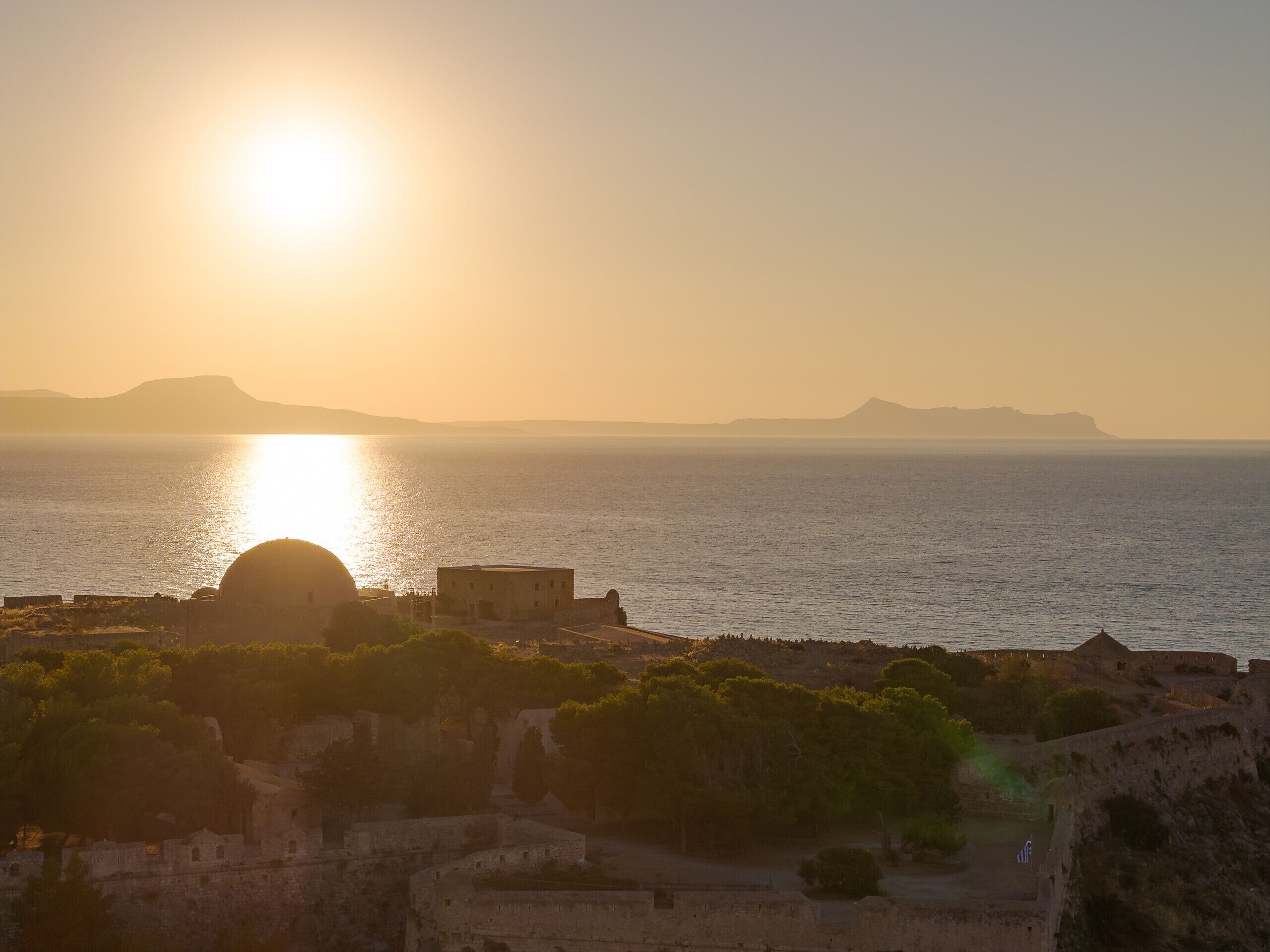 A coastal view with a sunset, a dome structure, and a fortified area with trees.