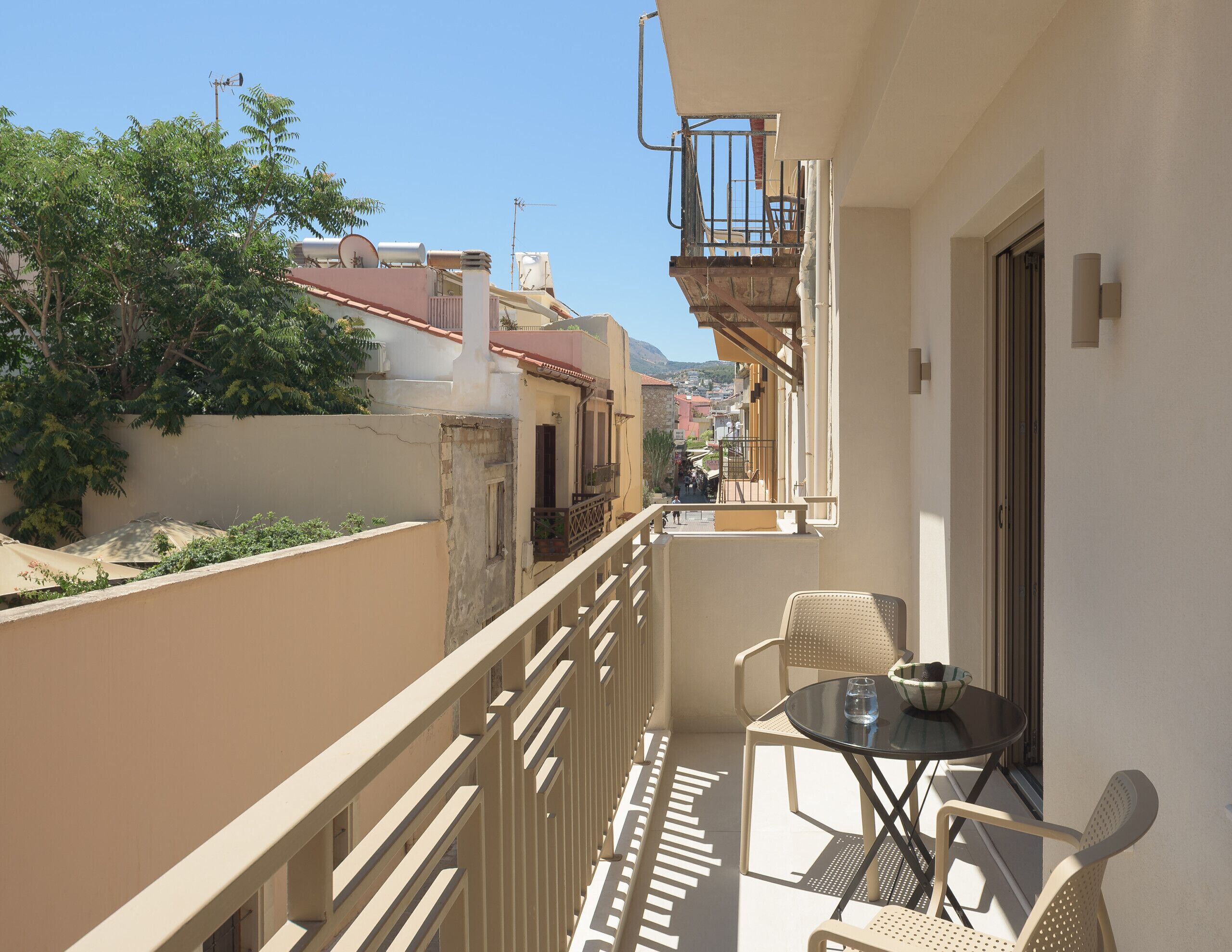 A balcony with a table and chairs, overlooking a street with buildings and a mountain in the distance.